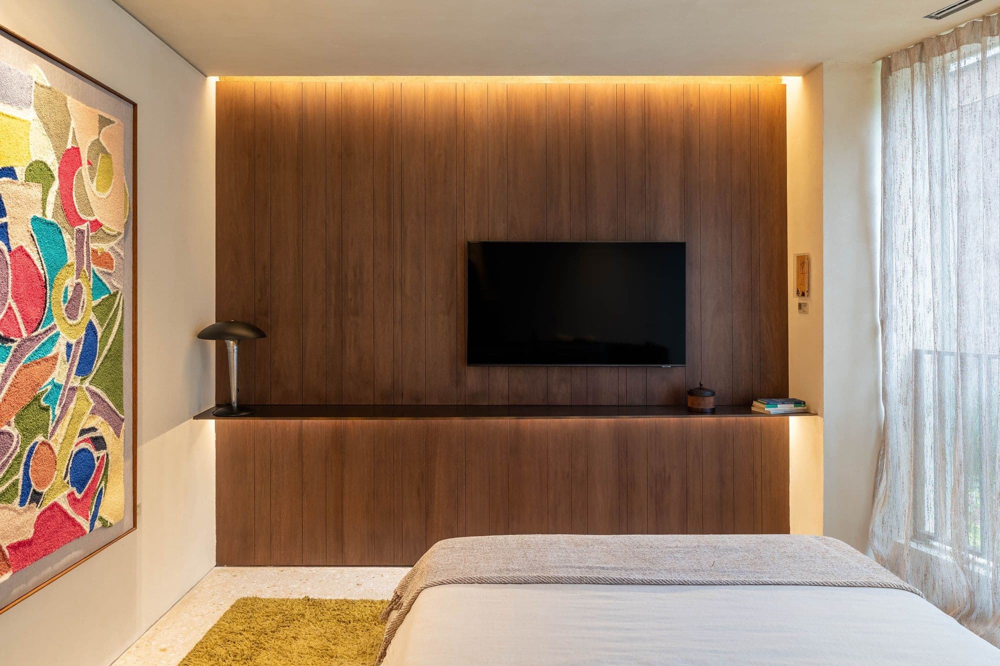 Quarto com painel de TV em lâmina de madeira e iluminação embutida no forro