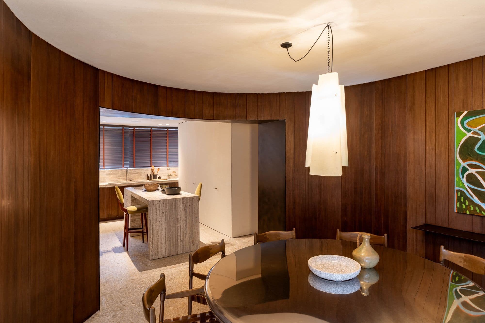 Sala de jantar circular revestida em madeira, com vista para a cozinha