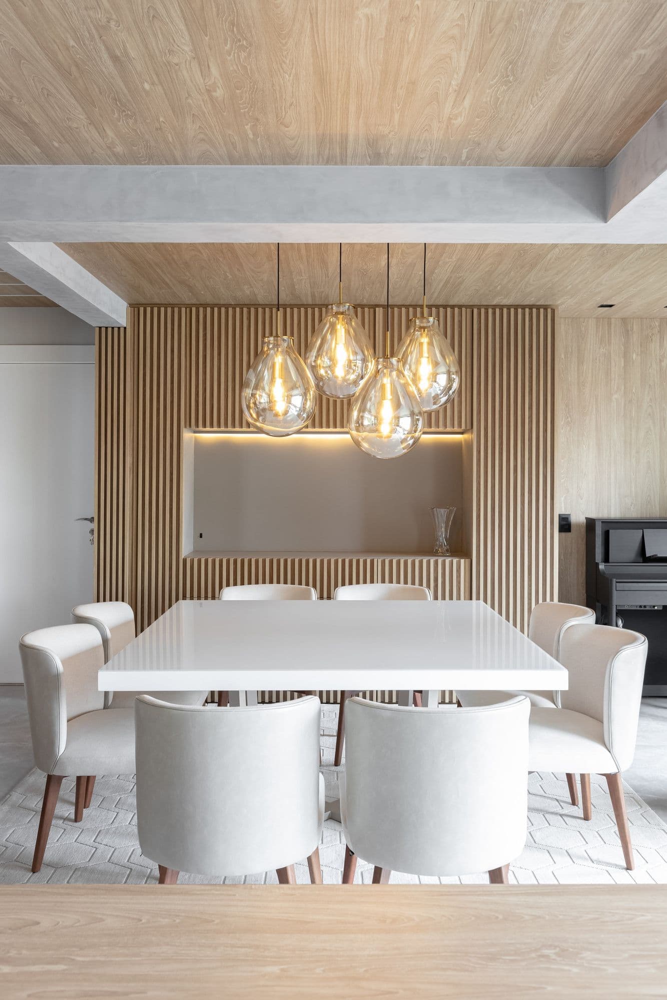 Sala de jantar com painel ripado iluminado e mesa branca para oito lugares