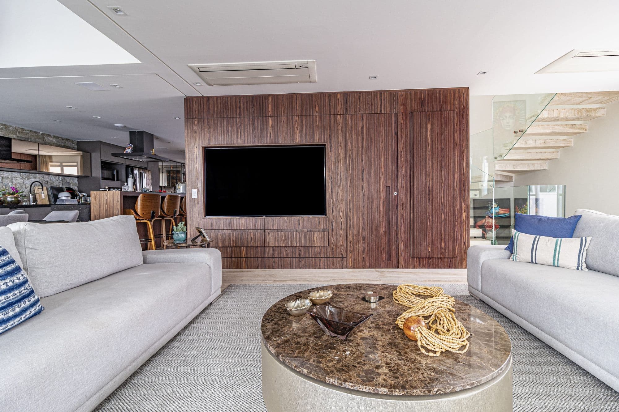 Sala de estar com painel de TV em lâmina de madeira escura e escada ao fundo