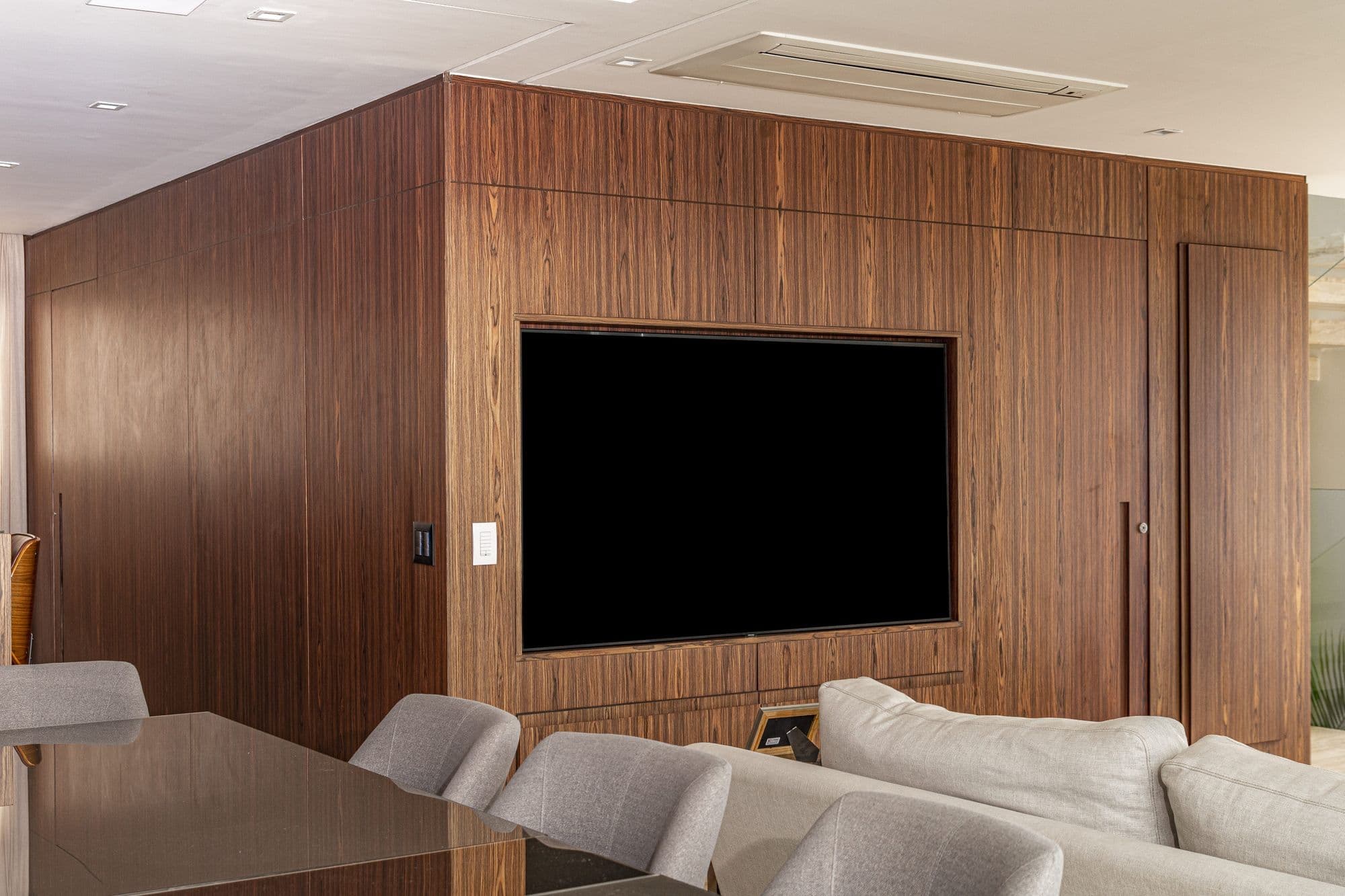 Volume em madeira escura com painel de TV visto da sala