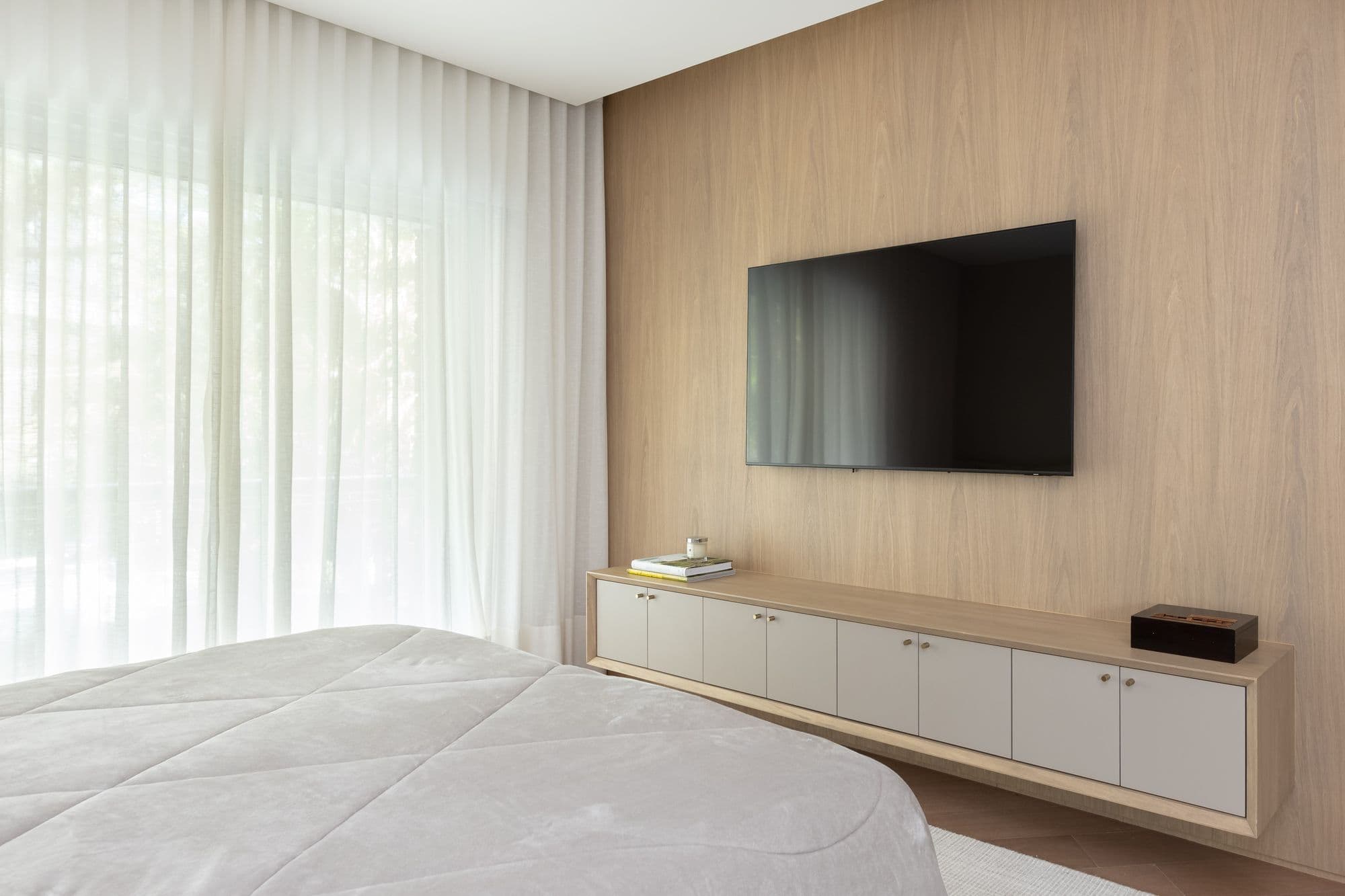 Quarto com painel de TV em madeira clara e rack suspenso