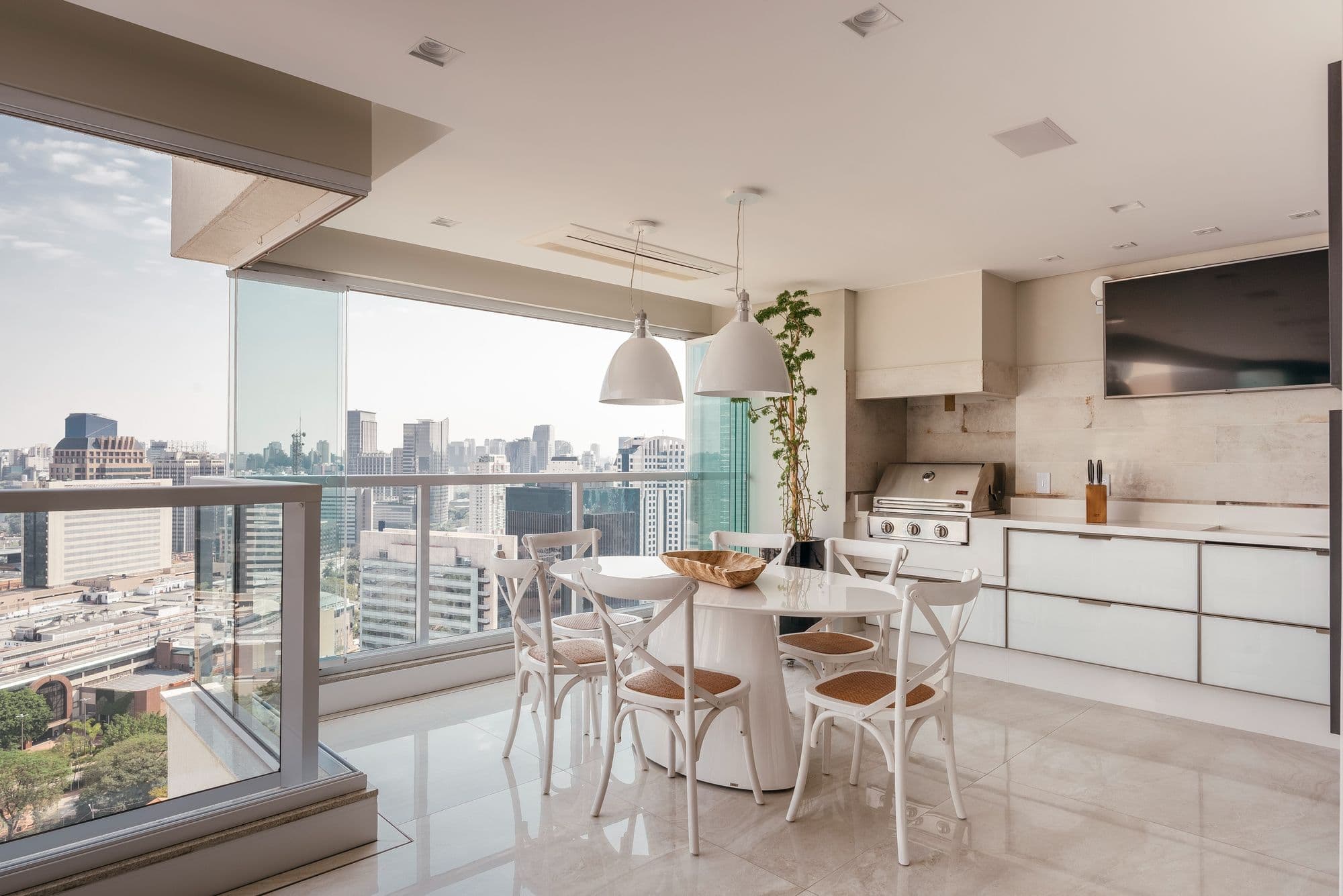 Varanda gourmet com cozinha planejada branca e vista da cidade