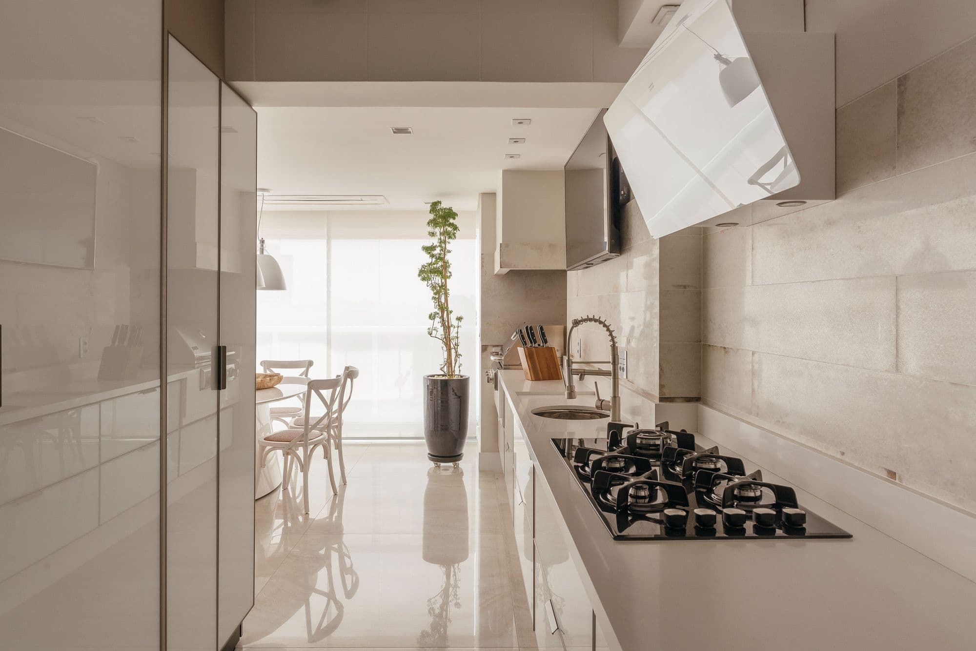 Cozinha linear branca com cooktop e janela ao fundo